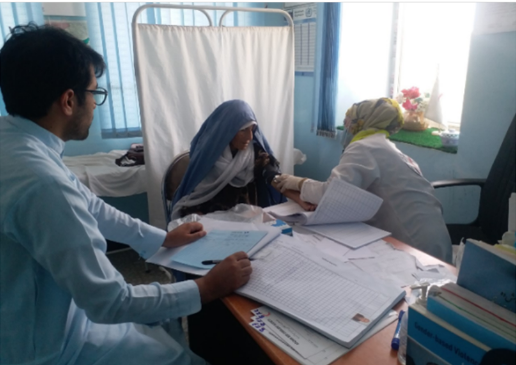 emro-afg-news-ncd-emergency-kit health worker provides care to patient another heath worker sat at a desk looking on