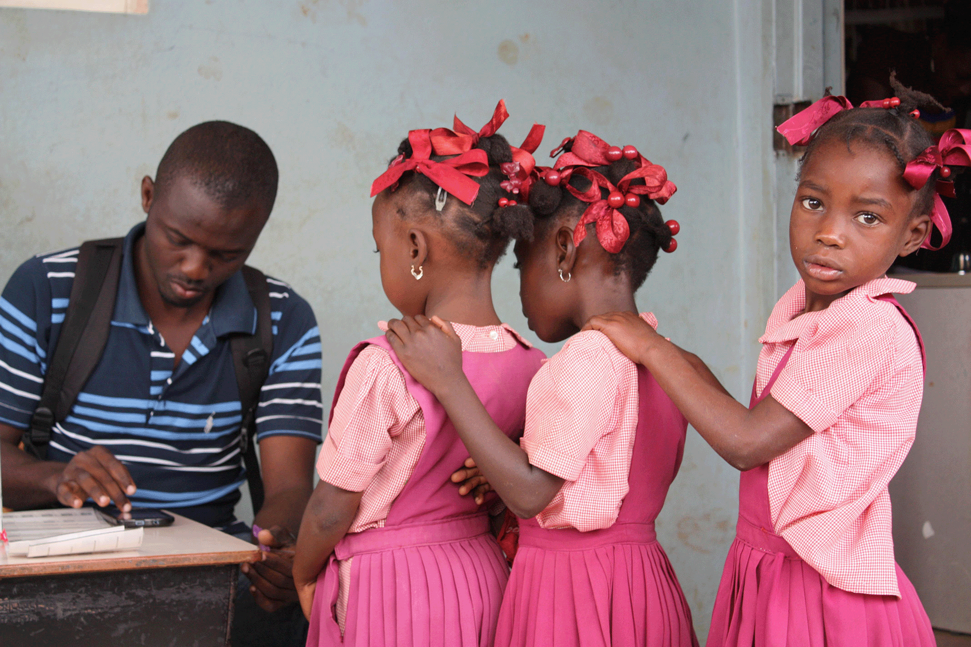 Disease detective conducts integrated transmission assessment surveys for LF of school children in Haiti Young girls stand in line in front of a desk where a man sits inputting data into a smartphone